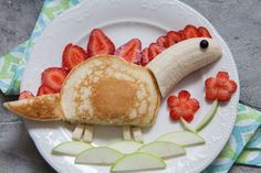 a plate topped with pancakes and sliced strawberries next to a banana shaped like a dinosaur