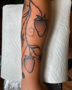 a woman's arm with tattoos on it and strawberries hanging from the branch