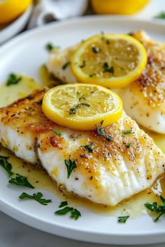 two fish fillets with lemon slices on a white plate