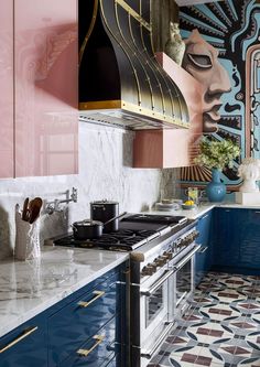 a kitchen with blue and pink cabinets, marble counter tops, and an oven hood