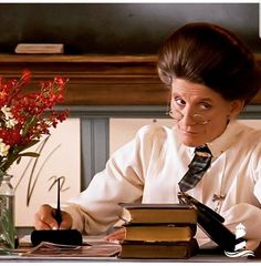 a woman sitting at a table with books and flowers