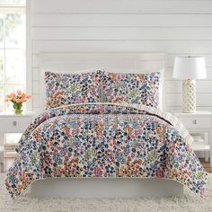 a bed in a room with white walls and a flowered comforter on it