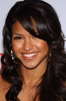 a smiling woman with long dark hair and large hoop earrings on her left ear, wearing a black dress