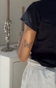 a man with a butterfly tattoo on his arm next to a white cabinet and two candles