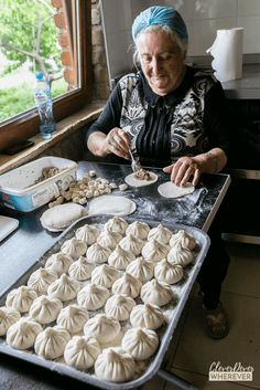 an older woman is making dumplings out of dough on a baking sheet in front of a window