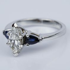 a diamond and blue sapphire engagement ring with two pear shaped diamonds on the side, set in white gold