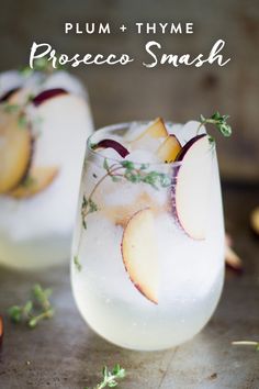 two glasses filled with ice and fruit on top of a table next to sliced apples