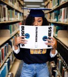 a woman is holding up a book in front of her face while standing in a library