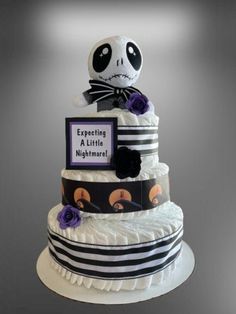 a three tiered cake decorated with black and white stripes, purple flowers and a jack skellingy face