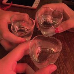 two hands holding glasses with water in them on a table next to a cell phone