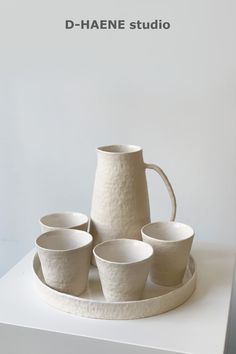 a white vase and four cups sitting on top of a table with the words d - haene studio above it