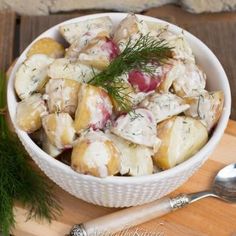 a white bowl filled with potato salad on top of a wooden cutting board next to a knife