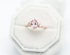 an oval shaped pink diamond ring with three diamonds on it's side in a white velvet box