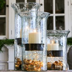 two glass vases with candles in them sitting on a table