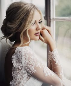 a beautiful blonde woman in a white dress looking out the window with her hand on her cheek