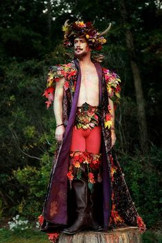 a man dressed up as a demon standing on top of a tree stump