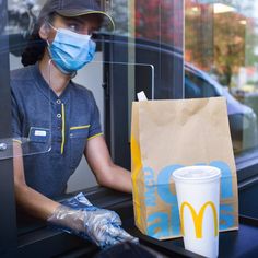 a woman wearing a face mask and gloves sitting at a mcdonald's restaurant window