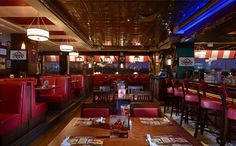 an empty restaurant with red booths and wooden tables in front of the bar, along with blue lights