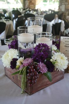 a wooden box filled with candles and flowers on top of a white table cloth covered table