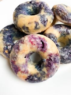 four doughnuts with blue and purple toppings on a white plate