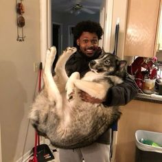 a man holding a large dog in his arms while standing next to a kitchen counter