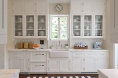 a white kitchen with lots of cabinets and counter space, including a clock on the wall