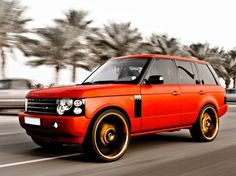 an orange range rover driving down the road with palm trees in the backgroud