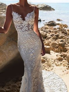 a woman in a wedding dress standing on rocks near the ocean