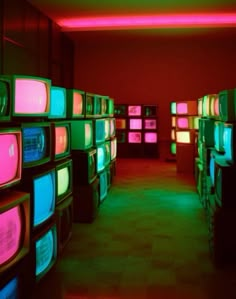 several televisions are stacked up in a room with red and green lights on the walls