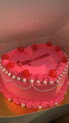 a pink heart shaped cake with cherries and pearls on the top is in a box