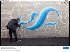 a man painting the side of a building with blue letters and swirls on it