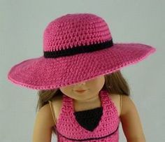 a doll wearing a pink crocheted hat with black ribbon around the brim