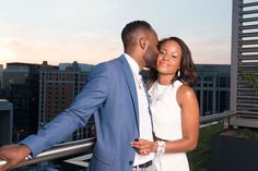 a man and woman standing next to each other on top of a roof with buildings in the background