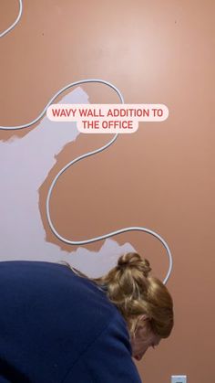 a woman sitting in front of a wall with a sign on it that says way wall addition to the office