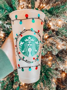 someone holding up a starbucks cup in front of a christmas tree with lights on it