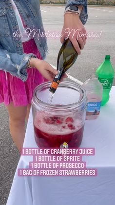 a woman pouring liquid into a glass jar with ice and strawberries on the table