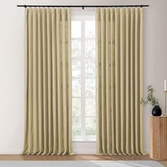 a living room with a large window covered in beige curtains and a rug on the floor