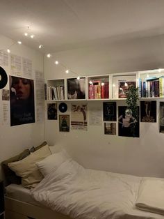 there is a bed with white sheets and pictures on the wall next to bookshelves