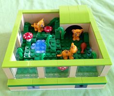 a toy house made out of legos with cats and mushrooms on the roof, sitting on a bed