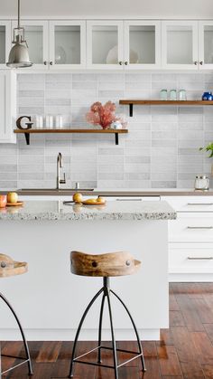 two stools sit in front of a kitchen island with white cabinets and open shelving