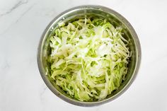 a metal bowl filled with shredded cabbage on top of a white marble countertop next to a knife