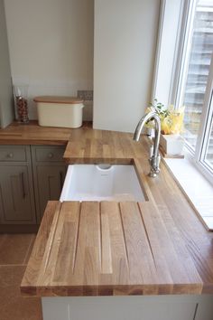 a wooden counter top sitting next to a white sink in a kitchen under a window