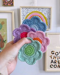 a hand is holding several crocheted flowers in front of pictures on the wall