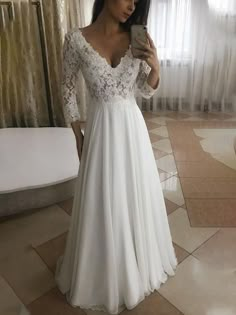 a woman in a white dress taking a selfie with her cell phone while wearing a lace and chiffon wedding gown