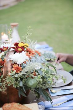 an arrangement of flowers on a table with plates and napkins in the foreground