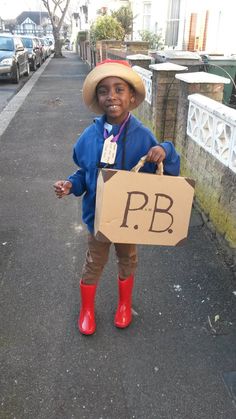 a young boy dressed in rain boots and holding a cardboard sign