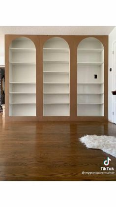 an empty living room with wooden floors and white bookcases