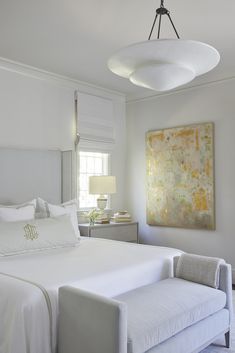 a white bedroom with a large painting hanging on the wall and a bed in front of it