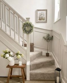 a white staircase with flowers and candles on the side table next to it, in front of some framed pictures