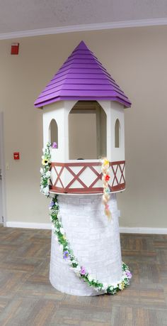 a purple and white tower with flowers on the top is in an empty room next to a door